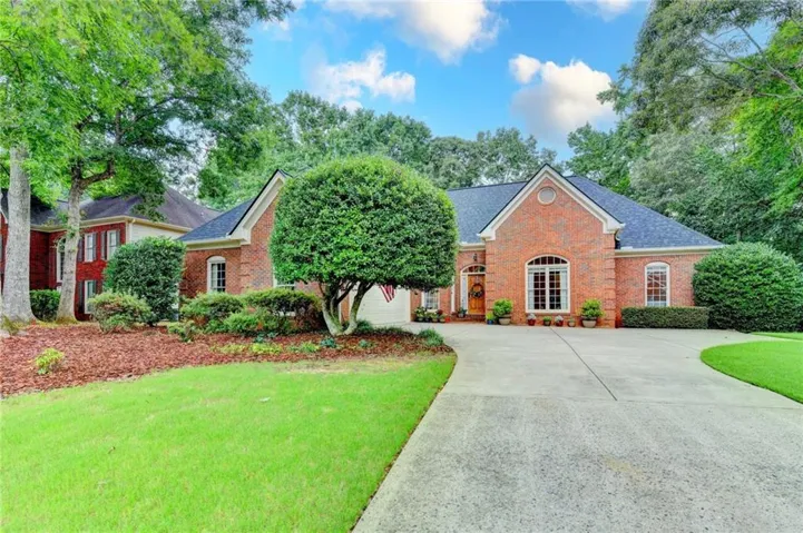 Brick exterior residence featuring a dark shingle roof, arched windows, and a concrete driveway
