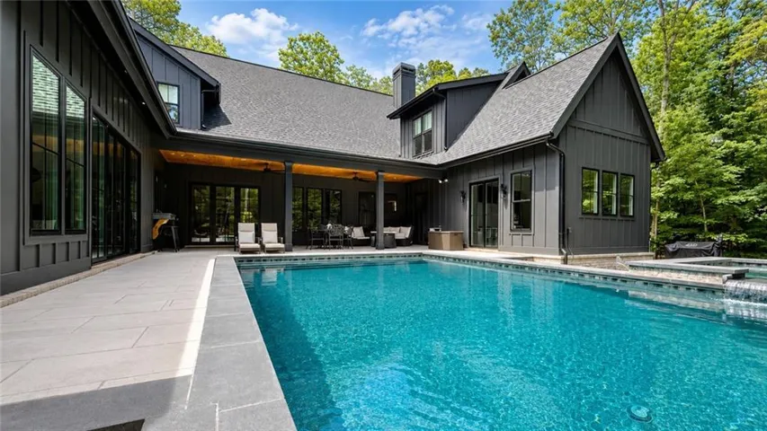 Expansive outdoor living area featuring a large swimming pool with integrated spa and waterfall, a spacious paved patio, and a covered porch with recessed lighting