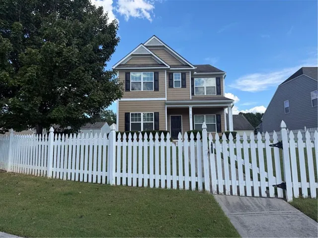 Two-story residence featuring a covered front porch, white picket fence, and dark window shutters