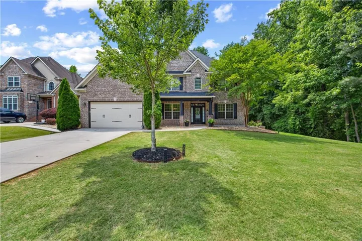 Brick facade residence featuring a two-car garage, covered entry, and lush front lawn with mature trees