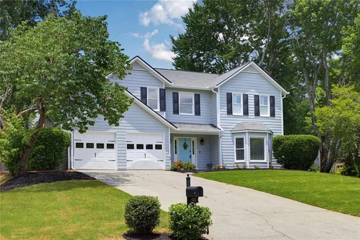 Two-story residence featuring light blue siding with dark shutters, a two-car garage, and a light blue entry door