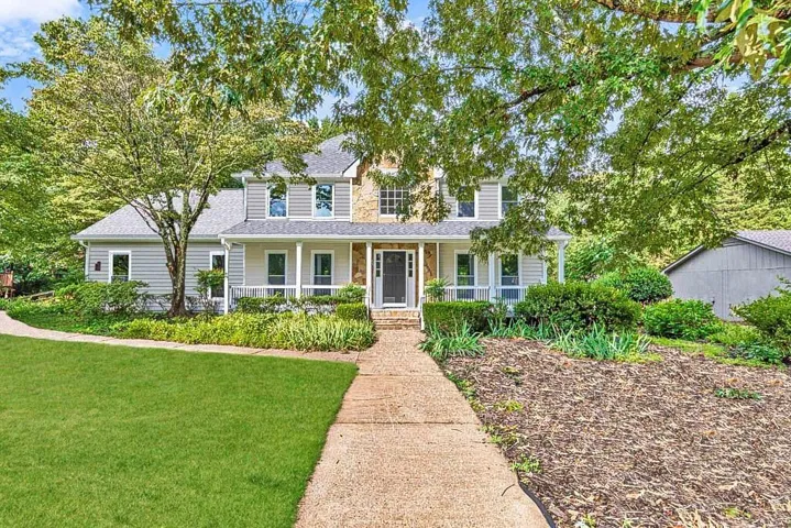 Two-story residence featuring a stone and siding exterior, covered front porch, and mature landscaping