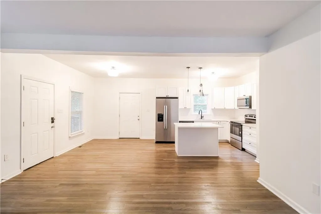 Kitchen with white cabinets, a center island, light countertops, stainless steel appliances, and hanging light fixtures