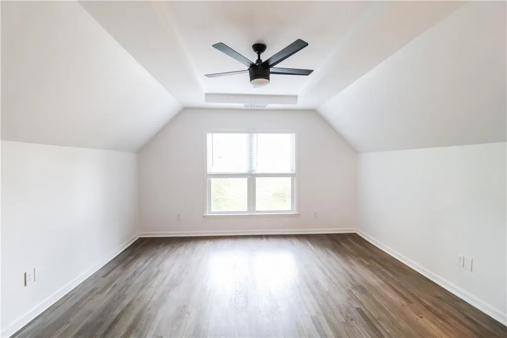 Additional living space with dark wood finished floors, vaulted ceiling, and a ceiling fan