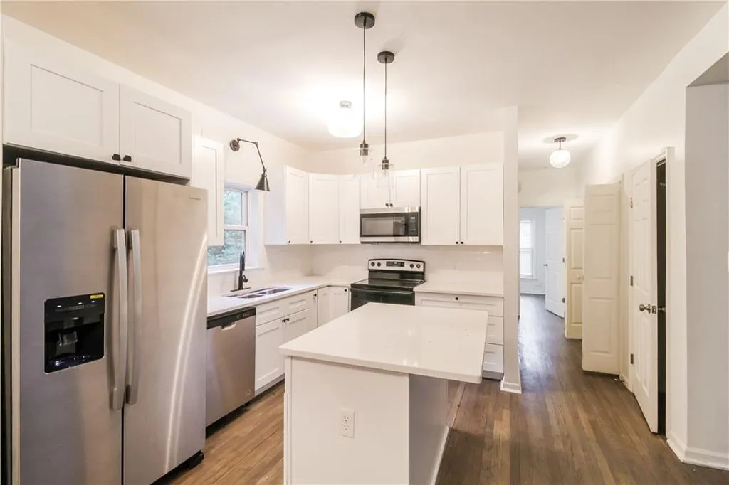Kitchen featuring stainless steel appliances, white cabinets, a center island, and dark wood-type flooring