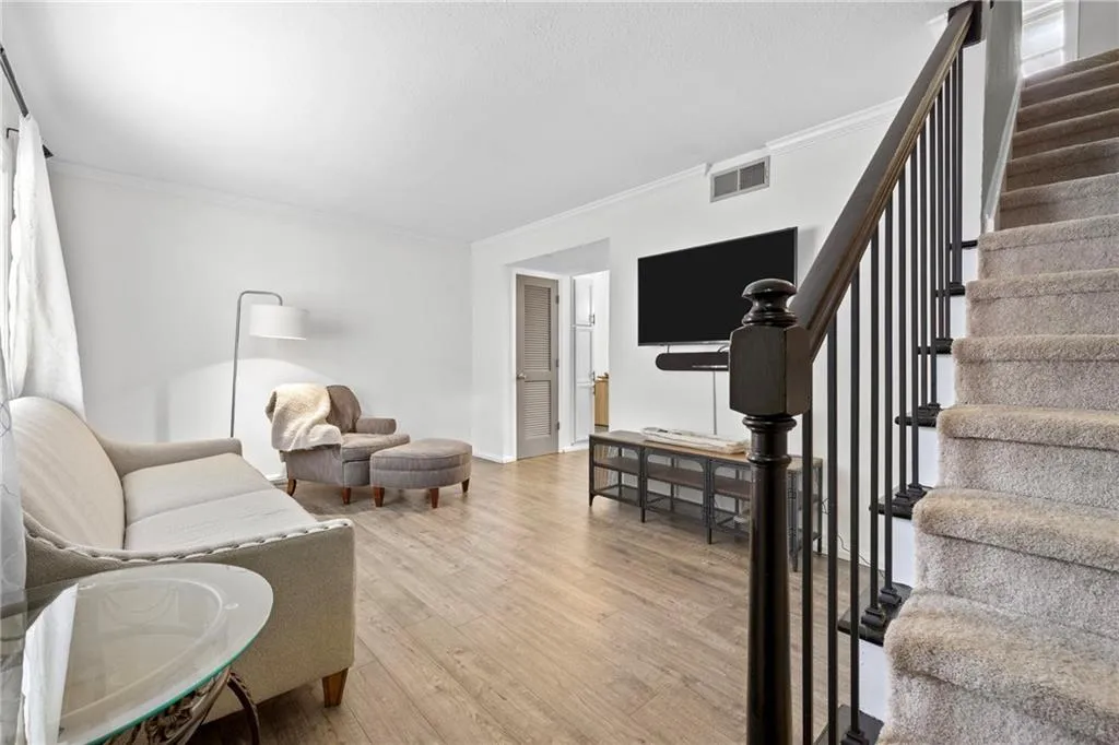 Living room with ornamental molding, light wood-style flooring, and stairway
