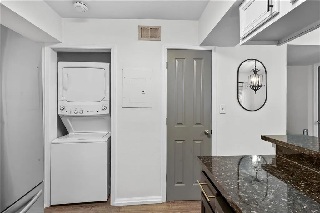 Laundry area with estacked washer and dryer, light wood-type flooring, and electric panel