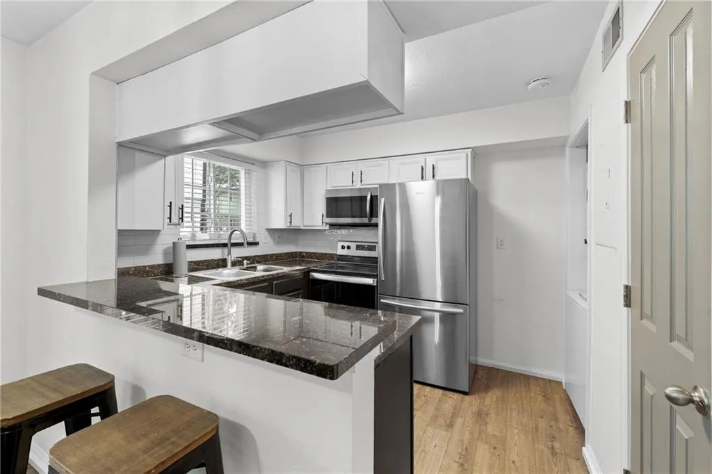 Kitchen featuring stainless steel appliances, a peninsula, a kitchen bar, white cabinets, and light wood finished floors
