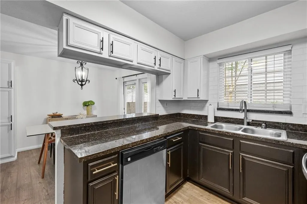 Kitchen with stainless steel dishwasher, dark brown cabinetry, white cabinetry, and light wood-style floors