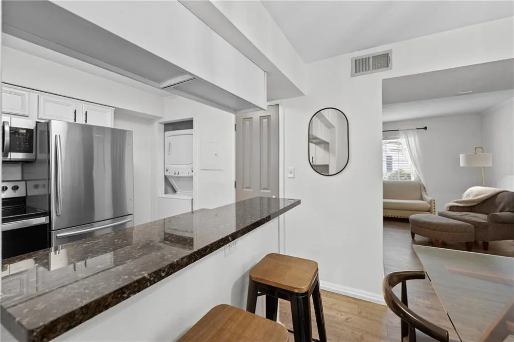 Kitchen with stacked washer / drying machine, appliances with stainless steel finishes, light wood finished floors, white cabinetry, and dark stone countertops