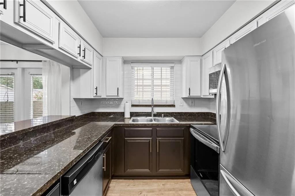 Kitchen featuring stainless steel appliances, white cabinets, dark stone countertops, light wood finished floors, and dark brown cabinetry