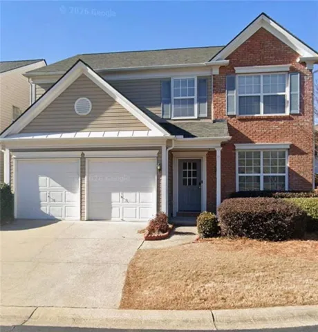 Exterior featuring a brick and siding facade, a two-car garage with panel doors, a covered entry, multiple windows with shutters, and a well-maintained front yard