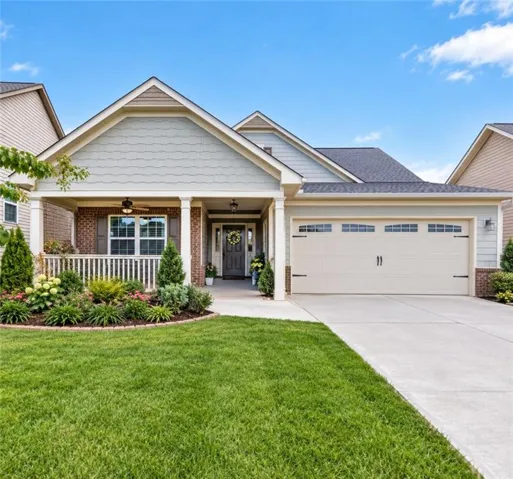 Covered front porch with brick accents, concrete driveway, attached two-car garage, and established landscaping