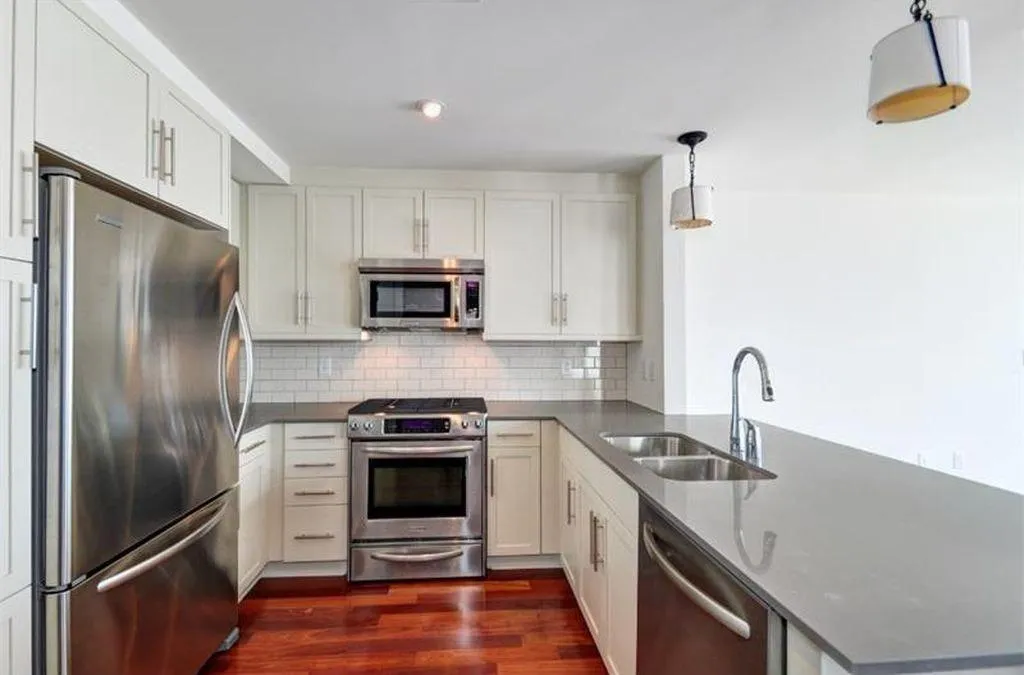 Kitchen with appliances with stainless steel finishes, hanging light fixtures, a peninsula, dark wood-style flooring, and dark stone countertops