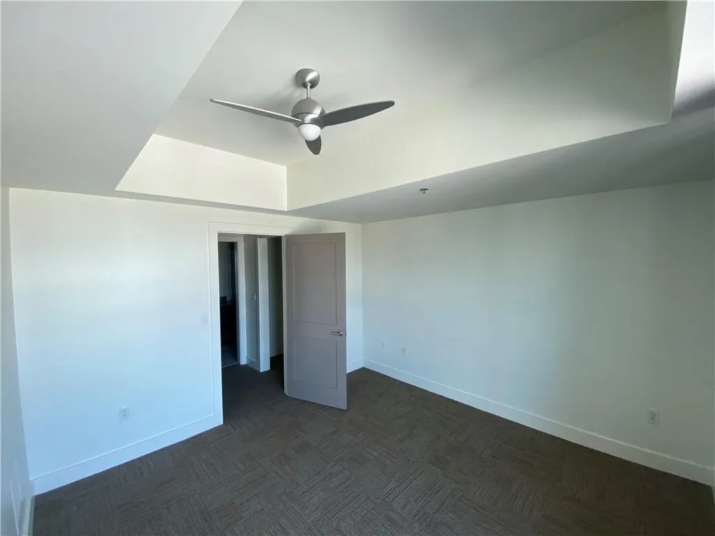 Unfurnished bedroom featuring dark carpet, a raised ceiling, and a ceiling fan