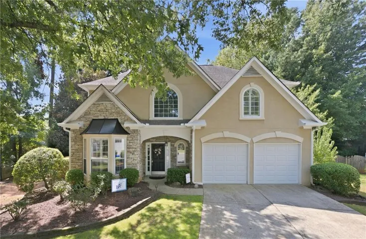 Stucco and stone facade with a bay window, a prominent arched window, and dual garage doors, complemented by mature landscaping