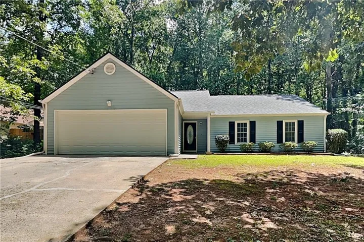 Single-story residence featuring light blue siding with white trim, an attached garage, a paved driveway, and a front yard with established landscaping