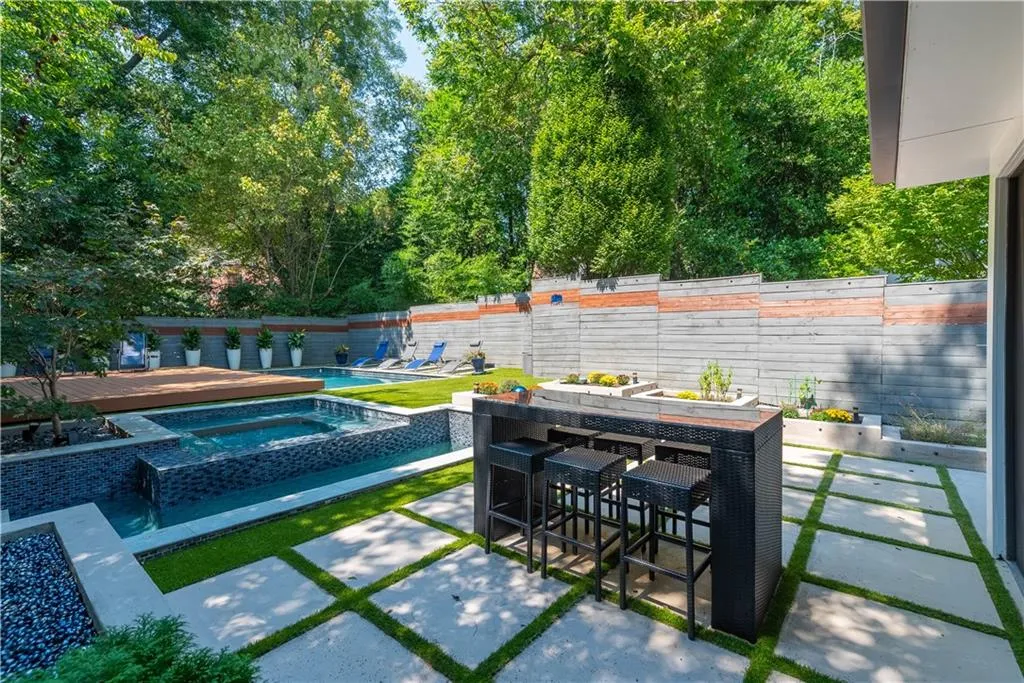 Outdoor entertaining area with pool, cascading hot tub, firepit, planters, dining area, and custom privacy fence