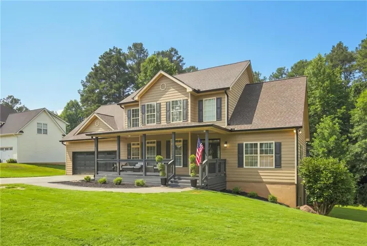 Siding exterior with dark shutters, covered front porch, attached two-car garage, and a sloped lawn