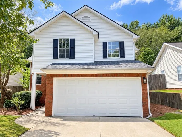 Two-story exterior featuring white siding and brick accents, an attached two-car garage, and a concrete driveway