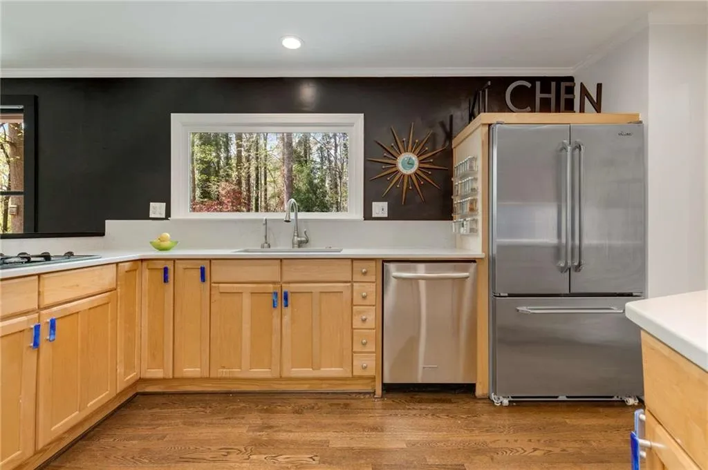 Kitchen with light countertops, crown molding, appliances with stainless steel finishes, a sink, and wood finished floors