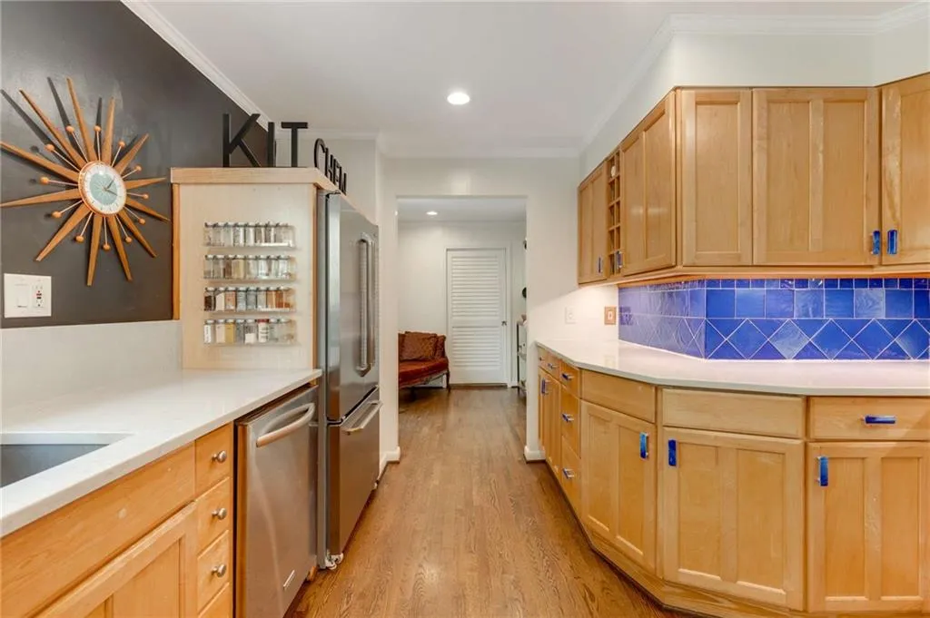 Kitchen with light wood-style flooring, appliances with stainless steel finishes, light countertops, and ornamental molding