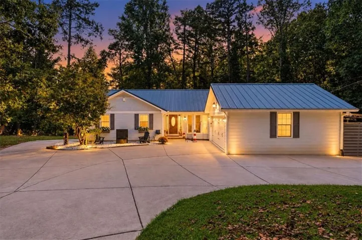 White siding exterior with a blue metal roof, an attached two-car garage, and a concrete drive