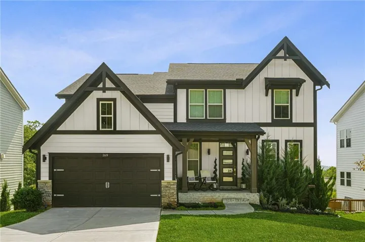 Modern farmhouse exterior featuring board and batten siding, dark trim accents, a covered front porch with wood columns, an attached two-car garage, and a manicured lawn