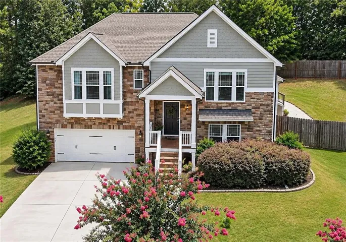 Stone and siding exterior with a covered entry, attached garage, and landscaped front yard