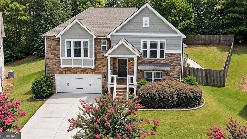 Two-story residence featuring a stone and siding facade, covered front entry, attached garage, and a fenced backyard