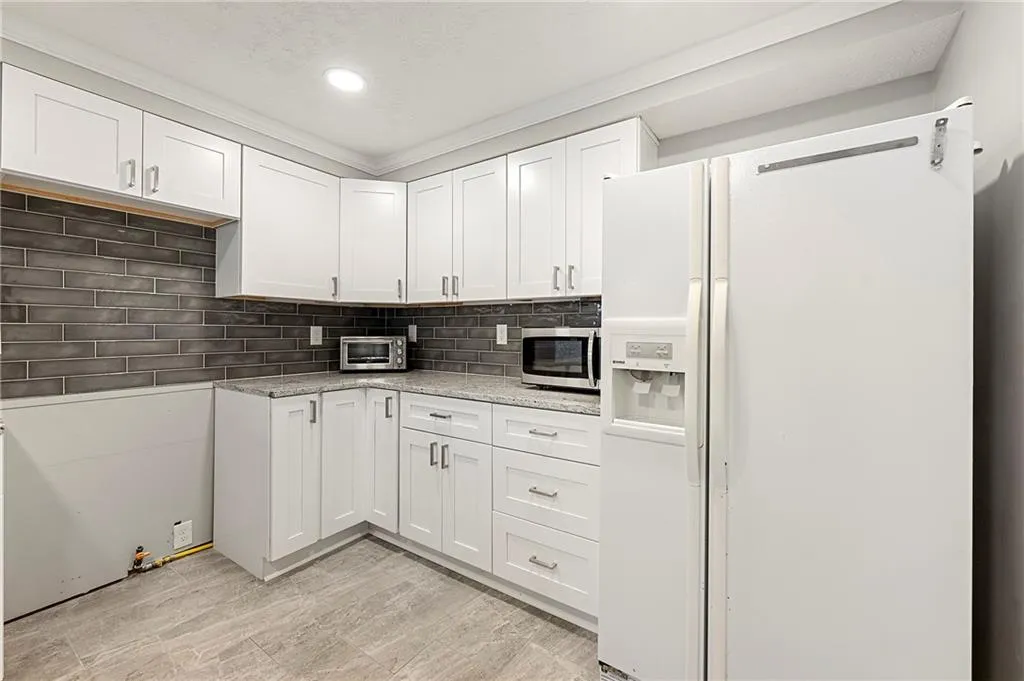 Kitchen with white refrigerator with ice dispenser, a toaster, tasteful backsplash, stainless steel microwave, and white cabinets