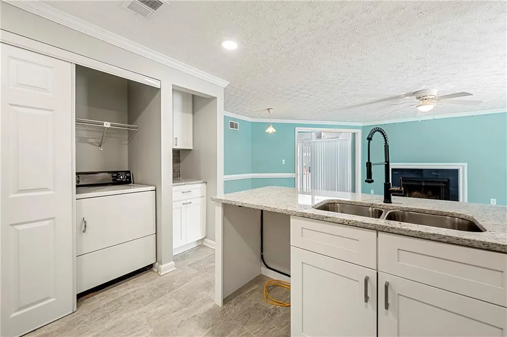Kitchen featuring washer / dryer, visible vents, white cabinets, light stone countertops, and a sink