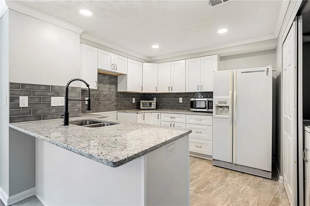 Kitchen featuring light stone counters, stainless steel microwave, white cabinetry, a sink, and white fridge with ice dispenser
