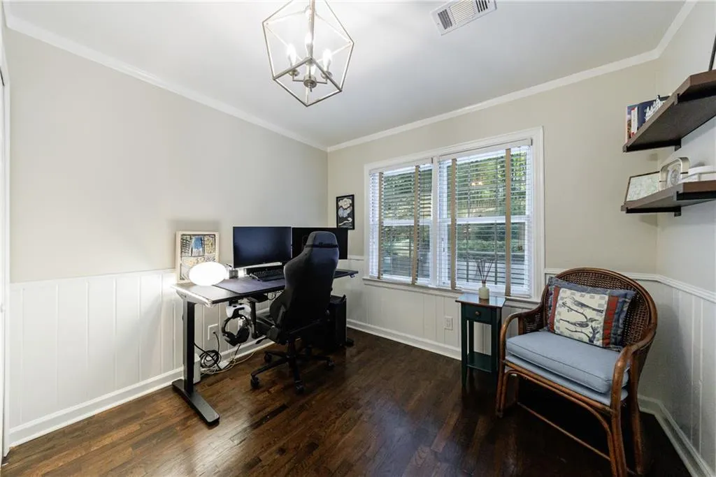 Office area featuring dark wood-type flooring, a chandelier, a wainscoted wall, ornamental molding, and a decorative wall