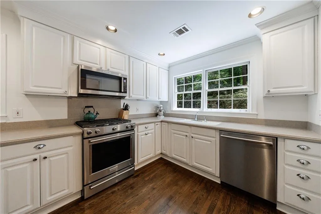 Kitchen with appliances with stainless steel finishes, dark wood finished floors, light countertops, crown molding, and white cabinets