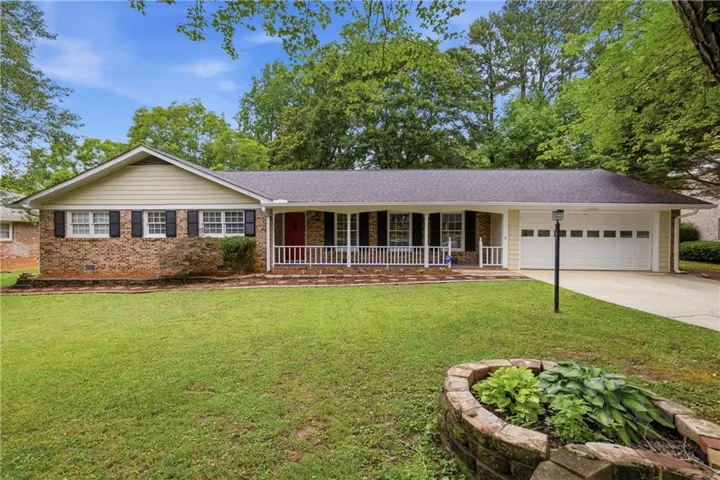 Brick and siding exterior with a dark shingle roof, featuring a covered front porch with white railings, a two-car garage, and a concrete driveway