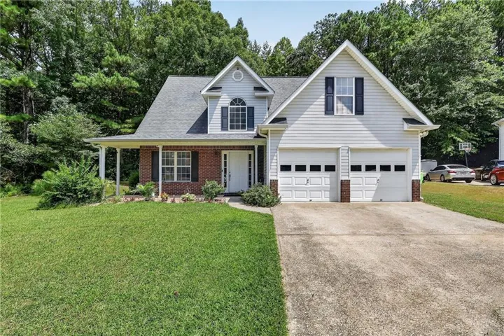 Two-car garage, covered front porch, brick facade, white siding, and mature landscaping
