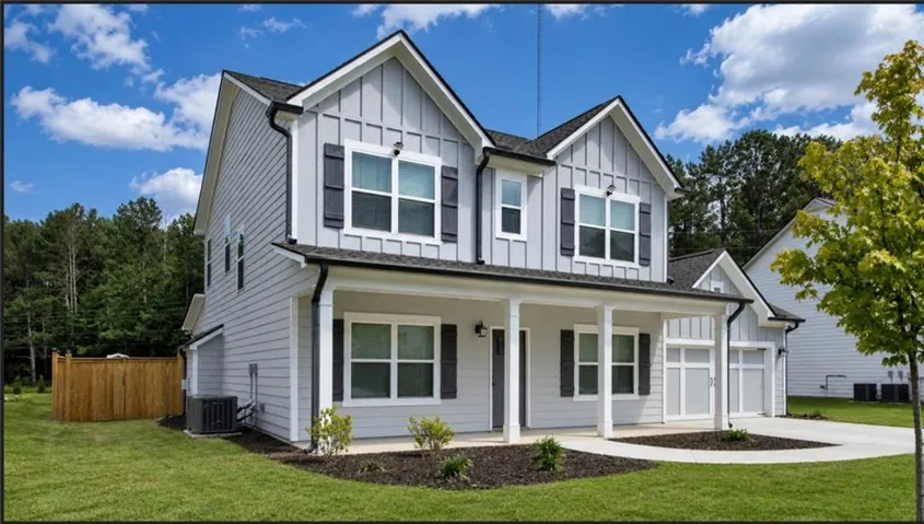 Modern farmhouse-style exterior featuring light gray board and batten siding, dark framed windows with shutters, a covered front porch with white columns, and an attached two-car garage