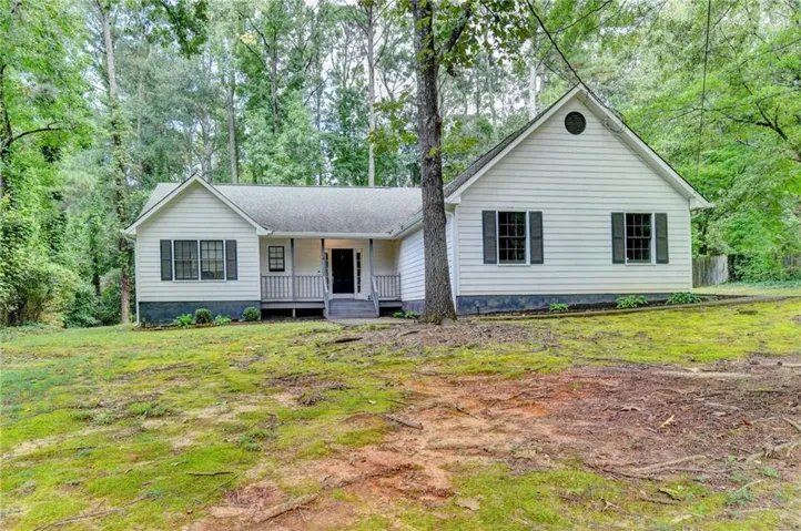 White siding exterior with dark shutters, front porch with railings, gabled roofline, and established trees