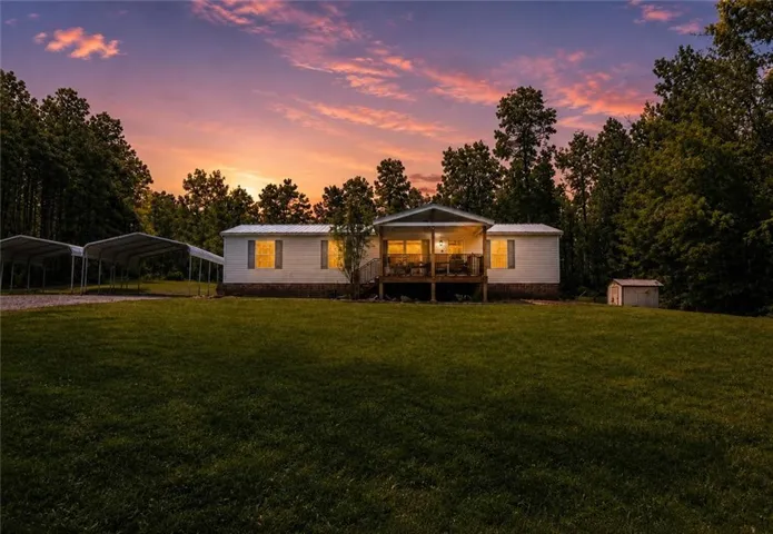 Expansive property featuring a residence with an elevated covered porch, two detached metal carports, a storage shed, and mature perimeter trees
