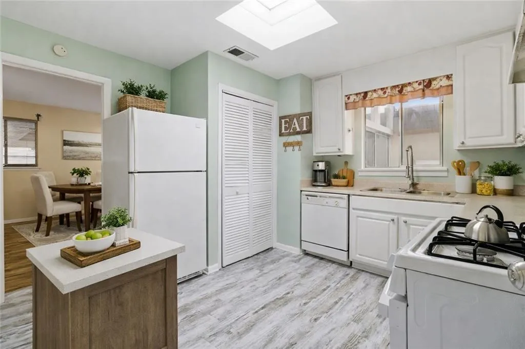 Kitchen featuring white appliances, a skylight, light wood-style floors, and white cabinets