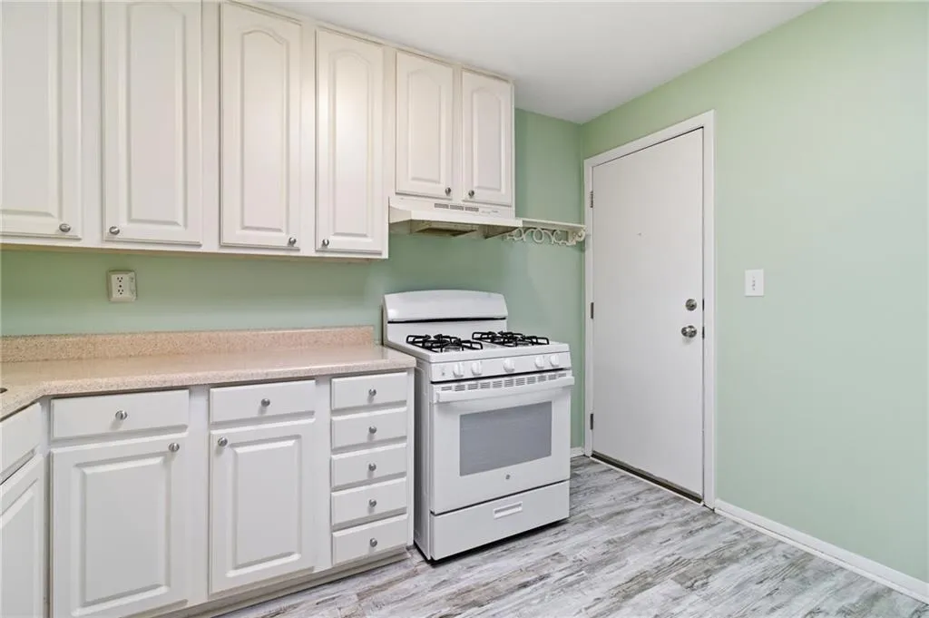 Kitchen with gas range gas stove, under cabinet range hood, white cabinets, and light wood-type flooring
