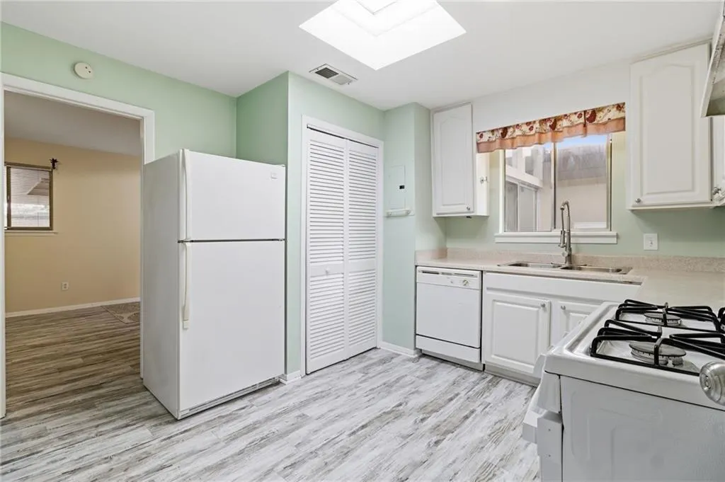 Kitchen with white appliances, light countertops, white cabinetry, and light wood-style flooring