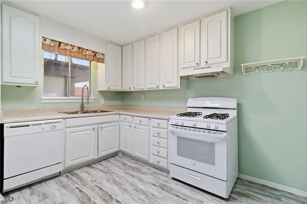 Kitchen with white appliances, light countertops, light wood-type flooring, under cabinet range hood, and white cabinetry