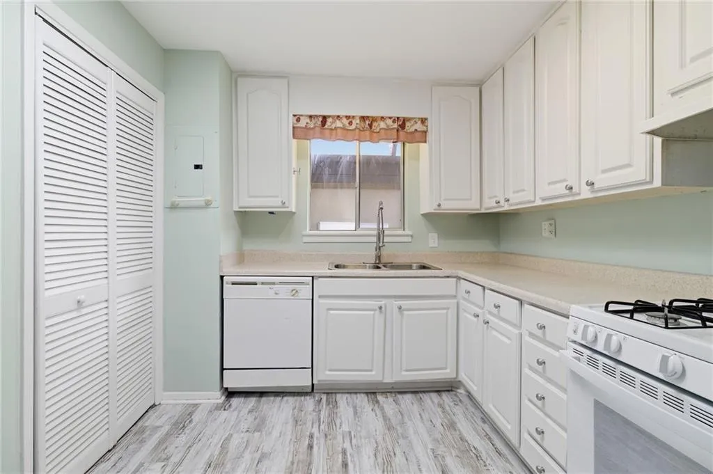 Kitchen with light countertops, white appliances, electric panel, white cabinets, and light wood-style flooring