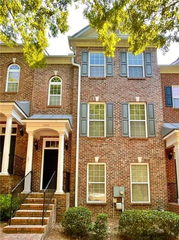 Brick exterior featuring multiple stories, a prominent front entrance with columns, dark shutters, and a mixture of arched and rectangular windows