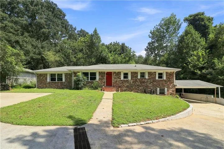 Brick exterior with white trim, a red front door, white window shutters, a covered carport, and a concrete driveway
