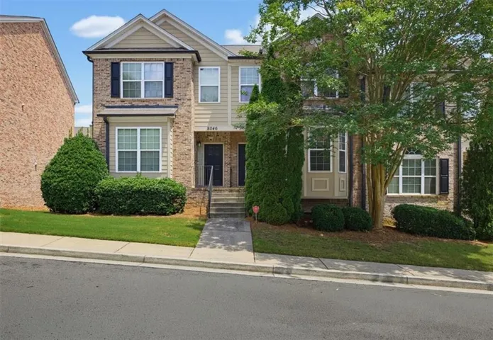 Multi-story townhome featuring brick and siding exterior, bay window, dark shutters, and manicured landscaping