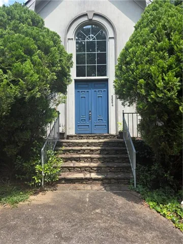 Architectural facade featuring an arched window, decorative blue double doors, and natural stone steps with metal railings