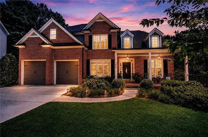 Brick exterior featuring a covered front porch with white columns, a two-car garage, and established landscaping